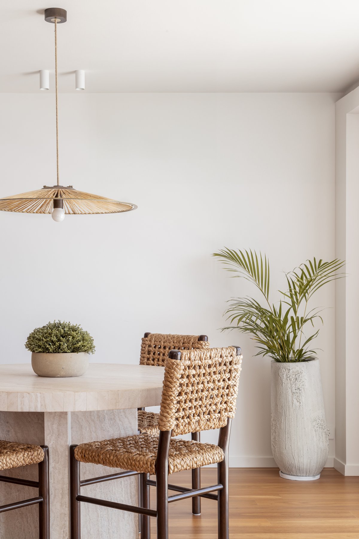 Dining nook with a round travertine table, woven timber chairs and a rattan pendant light
