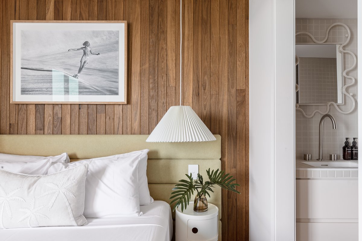 Bedroom with a timber-panelled feature wall, framed surf photography print, pendant light and a view through to the ensuite