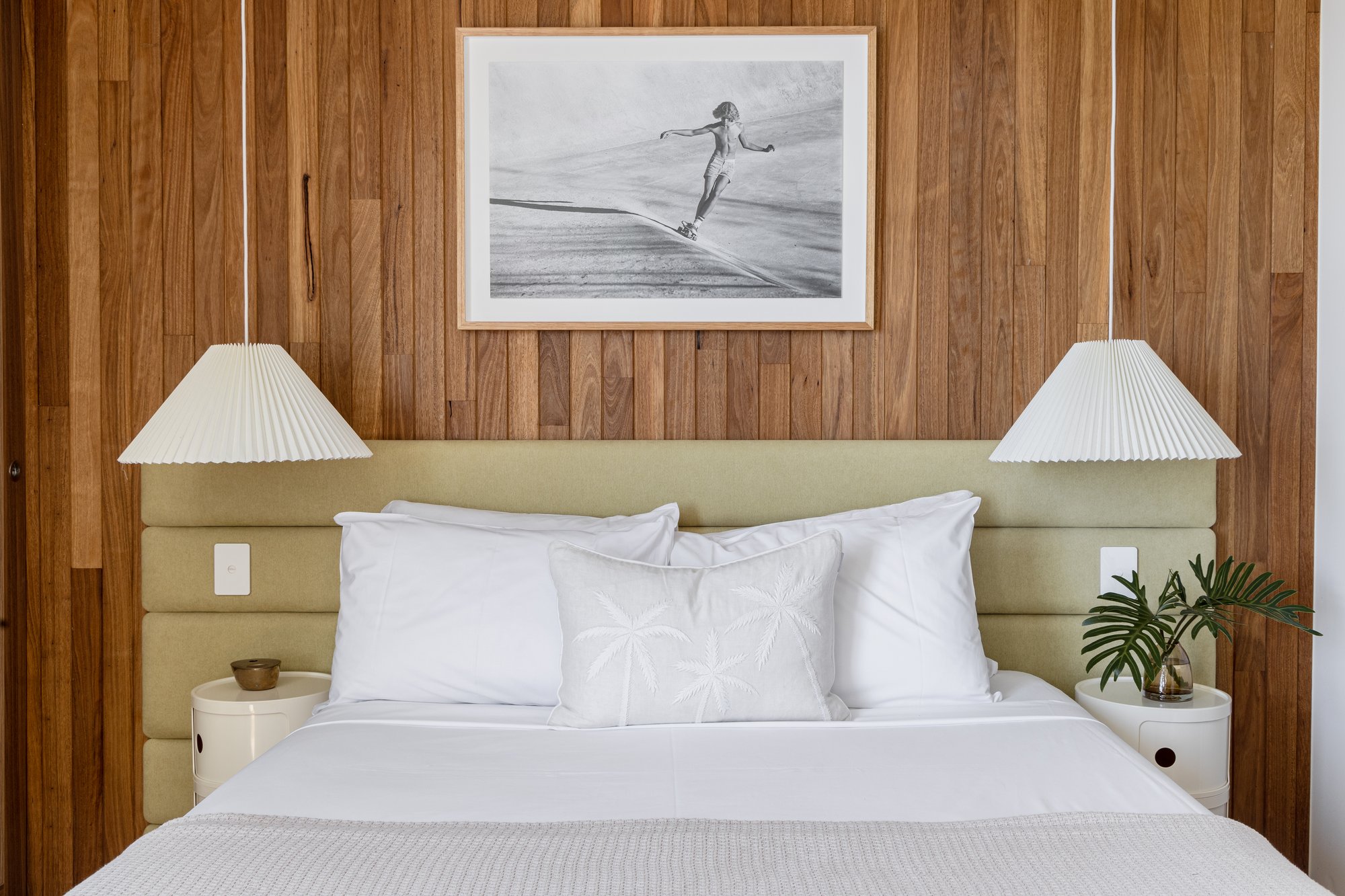 13B — bedroom with timber panelling, twin pendant lamps and framed surf photography above the headboard
