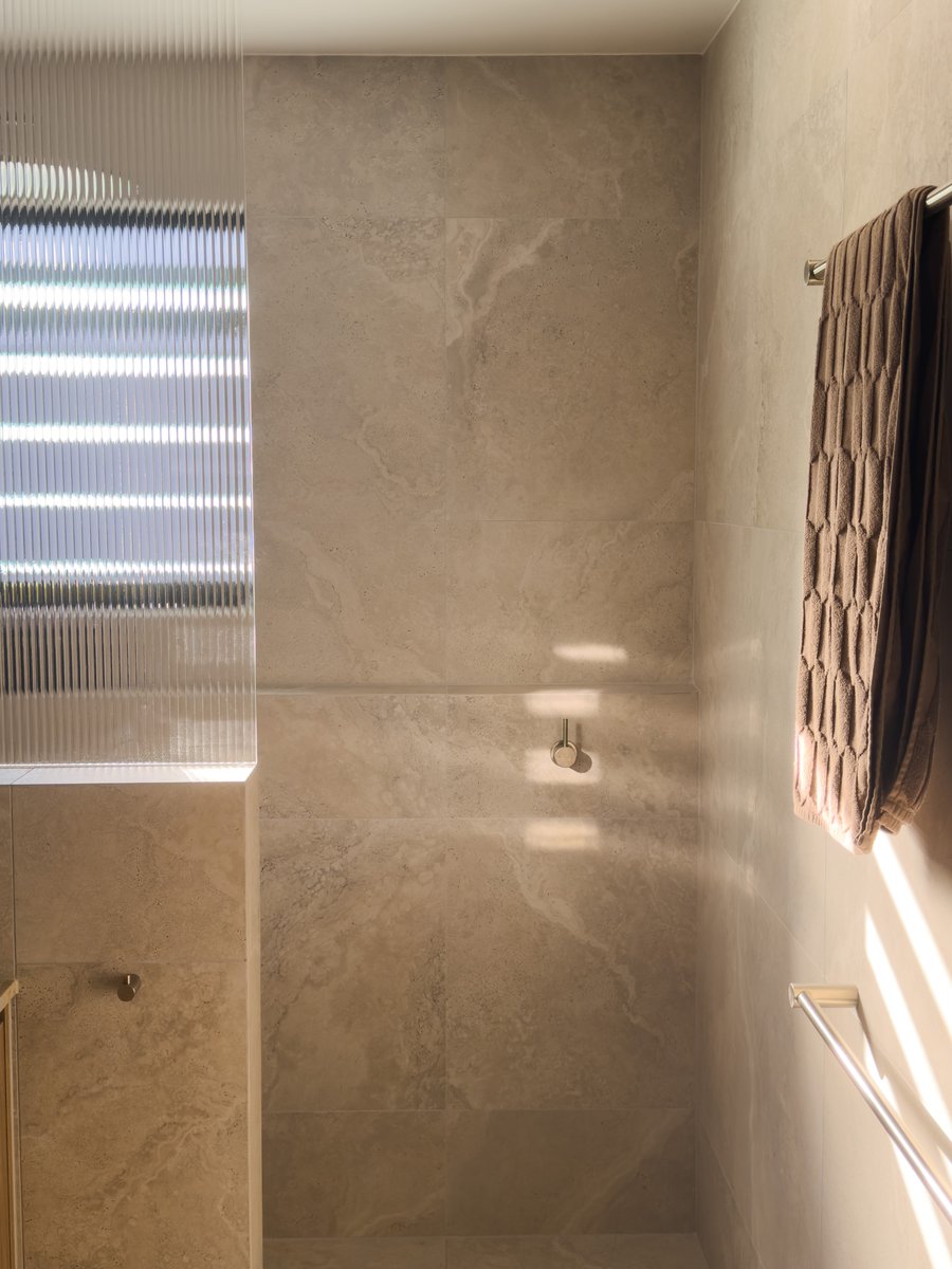Travertine-tiled ensuite with a reeded glass window, wall-mounted tapware and a towel rail